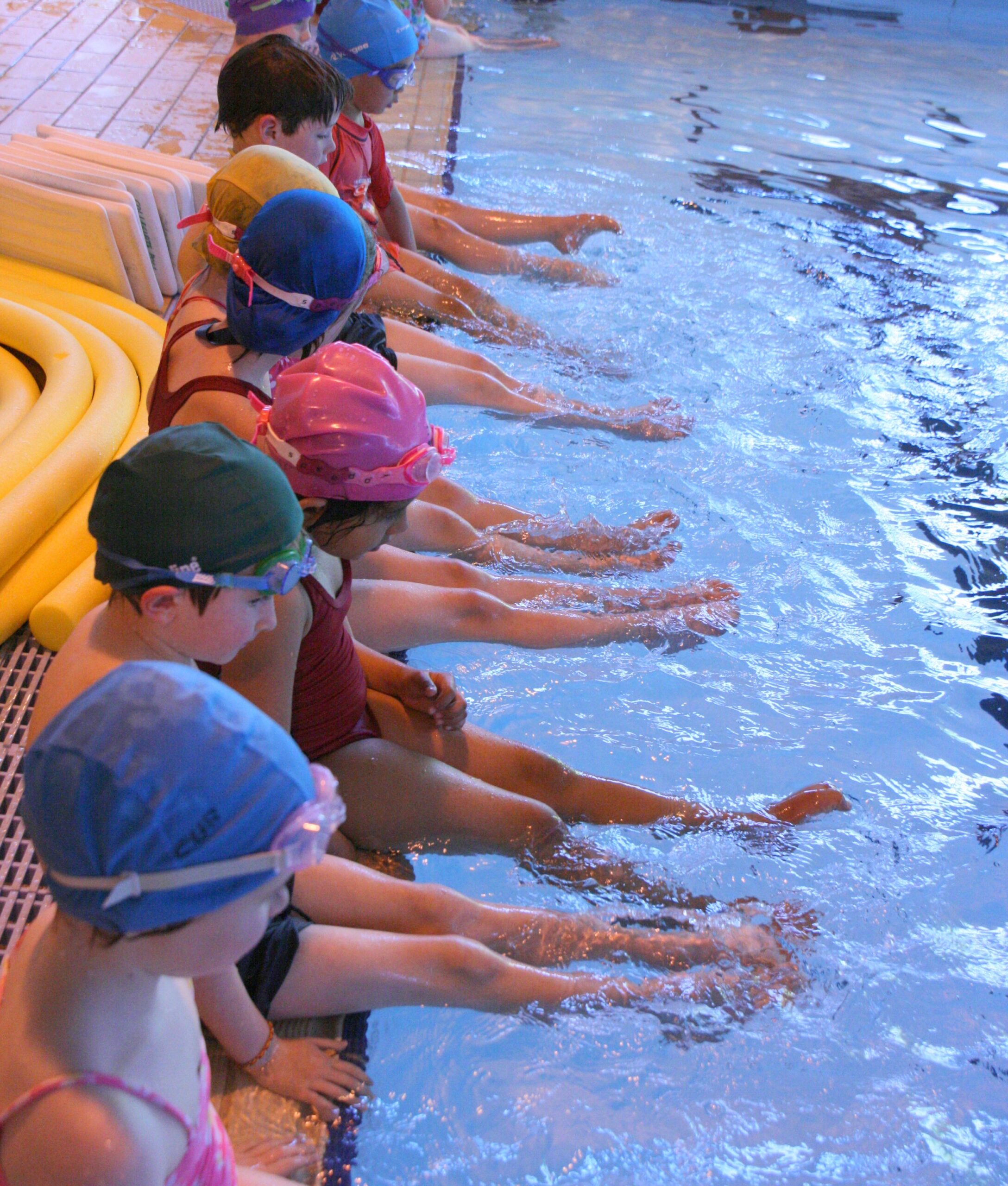 Swimmers on side of pool learning kicking legs.